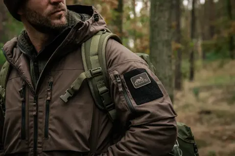 Mężczyzna w brązowej kurtce z naszywką Helikon-Tex, gotowy na przygodę. To dowód, że polskie marki outdoorowe to jakość i styl.