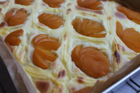 Wilgotne ciasto jogurtowe z budyniem i brzoskwiniami, pieczone w kwadratowej formie.