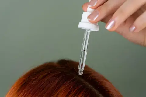 Kropla serum z pipety spada na rudą skórę głowy. Idealny sposób, czym natłuścić skórę głowy dla zdrowych włosów.