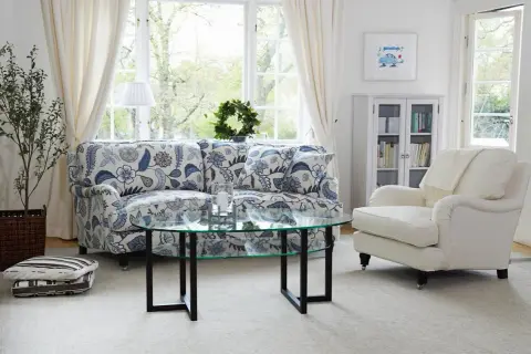 En ljus och inbjudande salong med en blommig Englesson fåtölj, soffa, soffbord och bokhylla.