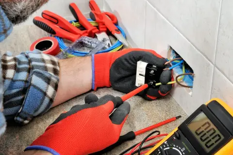 Un électricien utilise des outils pour installer une prise. On voit des fils, un tournevis, un multimètre et d'autres outils pour électricien.