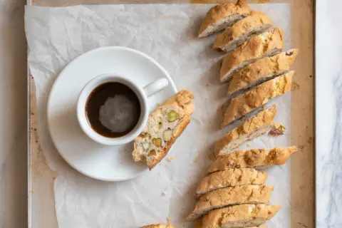 En kopp kaffe bredvid en rad med italiensk mandelskorpa, bakad med nötter och pistagenötter.
