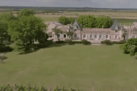 Un magnifique château bordelais, typique de la route des châteaux du Médoc, se dresse au milieu de vignes et d'arbres verdoyants.