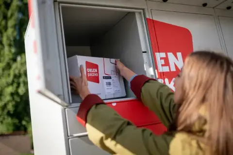 Kobieta wkłada paczkę do automatu ORLEN Paczka. Wymiary paczki są standardowe, pasują do skrytki.