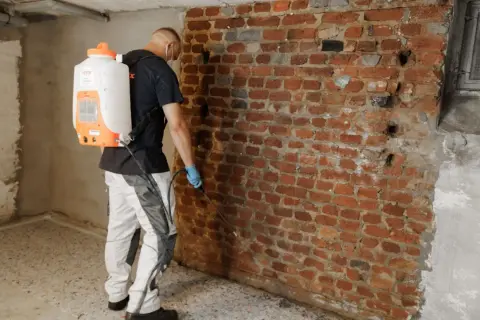Mann mit Sprühgerät dichtet Ziegelwand im Keller ab.