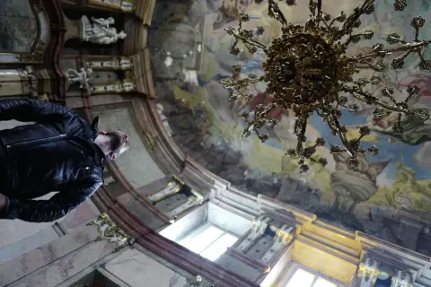 Mężczyzna w skórzanej kurtce podziwia freski i żyrandol w barokowym wnętrzu. Praga atrakcje zachwycają.