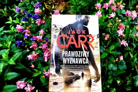 Prawdziwy Wyznawca" Jacka Carra, thriller w otoczeniu kwitnących kwiatów.