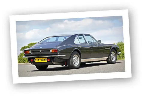 Klasyczny Aston Martin Lagonda w ciemnym kolorze, widziany z tyłu, na tle błękitnego nieba z chmurami.