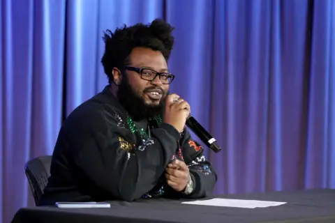 James Fauntleroy, a songwriter and producer, speaks into a microphone. His extensive James Fauntleroy discography is a testament to his talent.