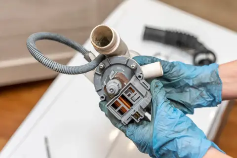 Naprawa pompy pralki, która nie odpompowuje wody. Widoczny element z wężem i złączem elektrycznym.