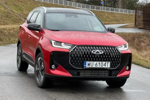 Czerwone auto Chery z czarnym grillem i felgami stoi na mokrej drodze.