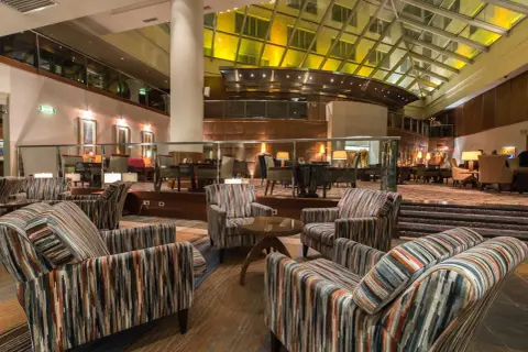 Przytulne fotele w paski w lobby hotelu Hyatt Warszawa, pod przeszklonym dachem.