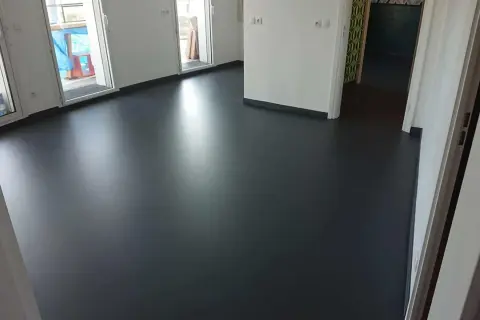 Un sol en résine époxy noir brillant, fraîchement posé, reflète la lumière dans un intérieur moderne.