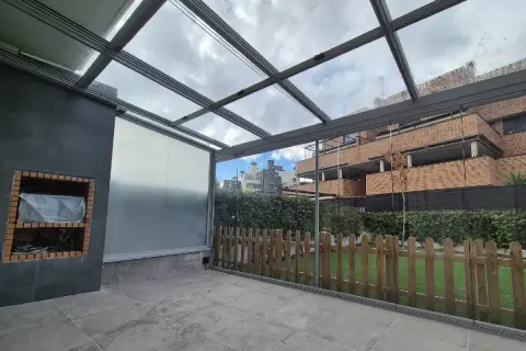 Patio con techo de cristal y estructura metálica, ideal para techar patio económico. Incluye barbacoa y valla de madera.
