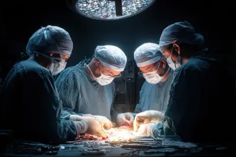 Zespół chirurgów w maseczkach i czepkach skupiony na skomplikowanej operacji pod jasnym światłem lampy.