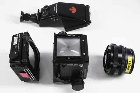 A Mamiya RZ67 camera body, film back, prism finder, and 110mm lens are laid out on a white surface.