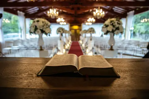 Otwarta Biblia na drewnianym stole, w tle ozdobiona sala. Liczba 7 w Biblii symbolizuje doskonałość i pełnię, jak w 7 dniach stworzenia.