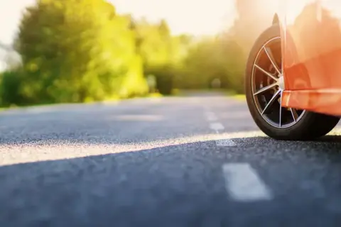 Pomarańczowy samochód na drodze, słońce przebija przez drzewa. Chcesz wiedzieć, jak szybko sprzedać samochód?