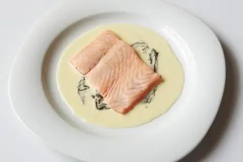 Deux pavés de saumon poêlés, nappés d'une onctueuse sauce oseille, servis sur une assiette blanche.