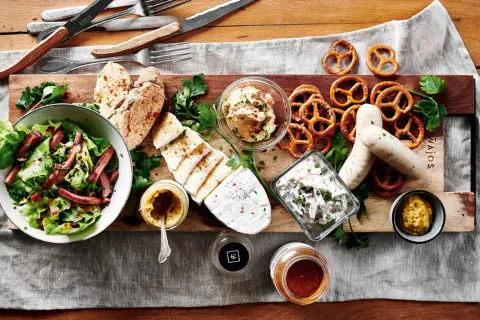 Herzhafte deutsche Gerichte: Wurst, Käse, Brezeln, Salat und Brot auf rustikaler Platte.