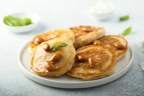 Pancakes con farina di mandorle, guarniti con mandorle intere e sciroppo dorato, su un piatto bianco.