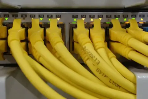 Conectores amarillos de red en un panel, cada uno con una luz verde o naranja encendida. Parece un splitter de red.