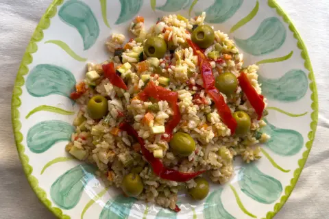 Deliciosa ensalada de arroz con pimientos rojos, aceitunas verdes y verduras picadas, servida en un plato decorado.