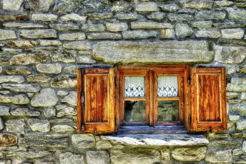 Ventana de madera con contraventanas abiertas, lista para restaurar. Cortinas de encaje blanco adornan los cristales.