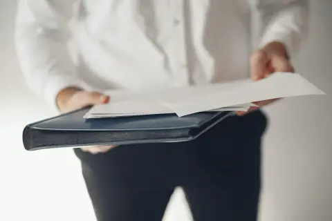 Osoba w białej koszuli trzyma teczkę z dokumentami, symbolizującą rezygnację z funkcji członka zarządu.