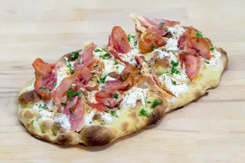 Une délicieuse pinsa recette garnie de burrata crémeuse, de fines tranches de prosciutto et de persil frais, le tout sur une pâte dorée.