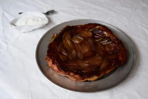 En gyllene lökpaj på en plåt, perfekt som lyxig mat att bjuda på. Serveras med en klick gräddfil.