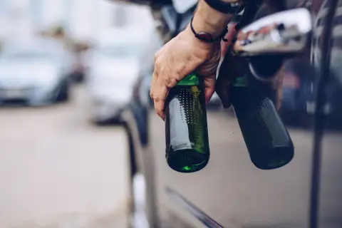 Hand hält Bierflaschen aus Autofenster. Die Frage "ab wie viel Promille ist man besoffen" wird hier thematisiert.