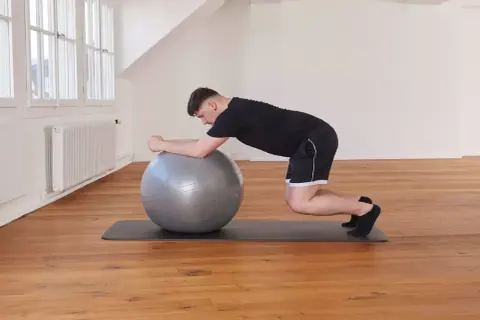 Un homme effectue un exercice de gainage avec un ballon de gym, en appui sur ses avant-bras et ses genoux.