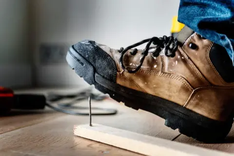 Buty robocze z podwyższonym noskiem chronią stopę przed gwoździem wbitym w deskę.