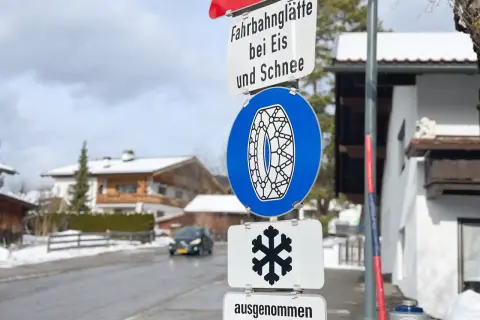 Verkehrsschilder weisen auf Fahrbahnvereisung bei Eis und Schnee hin. Ein blaues Schild zeigt eine Schneekette, ein weiteres ein Schneeflockensymbol.