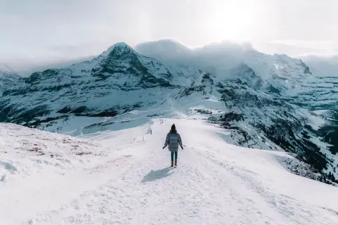 Une personne marche sur un sentier enneigé, dominant des montagnes majestueuses. Un paysage hivernal à couper le souffle, typique d'Interlaken, Suisse.