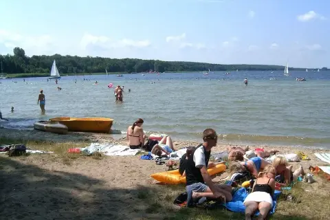 Ludzie odpoczywają na plaży, pływają i żeglują. To typowe **Boszkowo atrakcje** w słoneczny dzień.