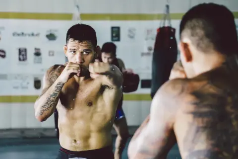 A fighter trains in a gym, punching the air. Can you go the same way twice in shadow boxing? He's focused, sweat glistening.