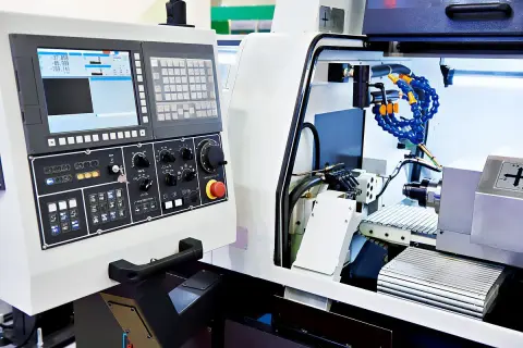 Panel sterowania zaawansowanych maszyn CNC z ekranem, klawiaturą i pokrętłami. Widać fragment obrabianego detalu i system chłodzenia.