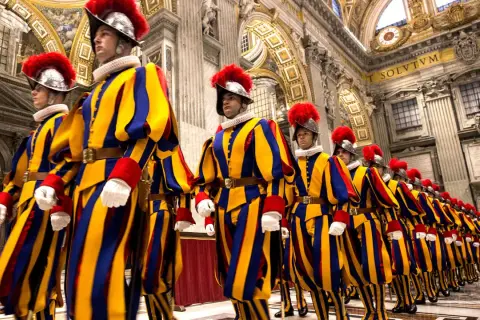 Guardia suiza del Vaticano desfila en formación, con sus icónicos uniformes a rayas amarillas, azules y rojas, y penachos rojos.