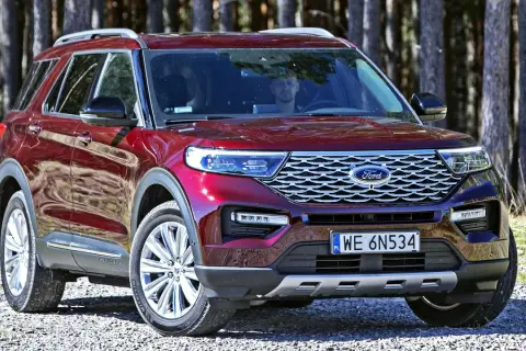 Czerwony Ford Explorer, jeden z wielu modeli tej marki, zaparkowany na leśnej drodze.