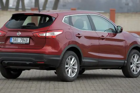 Czerwony Nissan Qashqai 2015 z czeskimi tablicami rejestracyjnymi stoi na brukowanym placu.