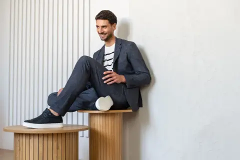 Uśmiechnięty mężczyzna w granatowym garniturze i pasiastym T-shircie, prezentujący styl smart casual.