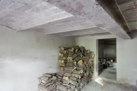 Widok stropu Kleina w przekroju, z widocznymi pustakami ceramicznymi i belkami. Obok stos drewna opałowego.