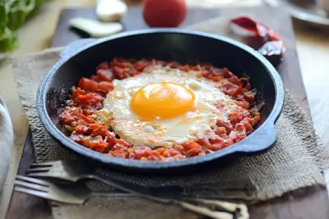 Un huevo frito sobre una cama de tomate picado en cazuelitas de aperitivo, listo para disfrutar.