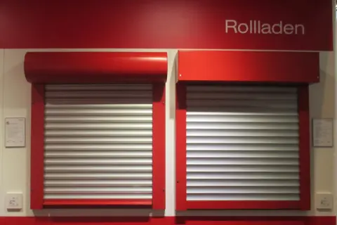 Dwie czerwone rolety zewnętrzne z aluminiowymi lamelami, prezentujące rozwiązania do ocieplenia domu.