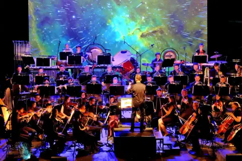 Orkiestra symfoniczna wykonuje najlepszą muzykę filmową wszech czasów na tle kosmicznej projekcji.