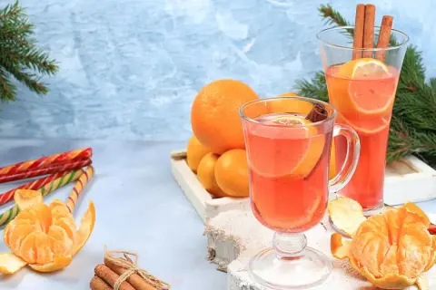 Zwei Gläser mit einem heißen Aperol-Getränk, garniert mit Orangen und Zimt. Daneben Mandarinen, Zuckerstangen und Tannenzweige.