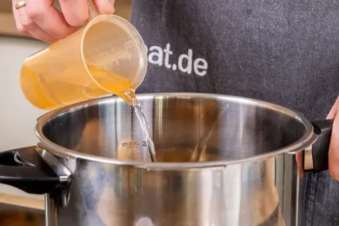 Flüssigkeit wird in einen Schnellkochtopf gegossen, bereit für die Zubereitung von Kartoffeln.