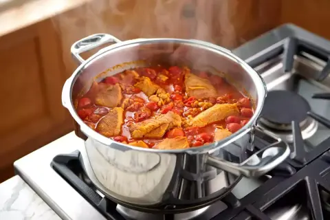 Un délicieux saute de porc mijote dans une cocotte en acier inoxydable sur une cuisinière à gaz, dégageant une vapeur appétissante.